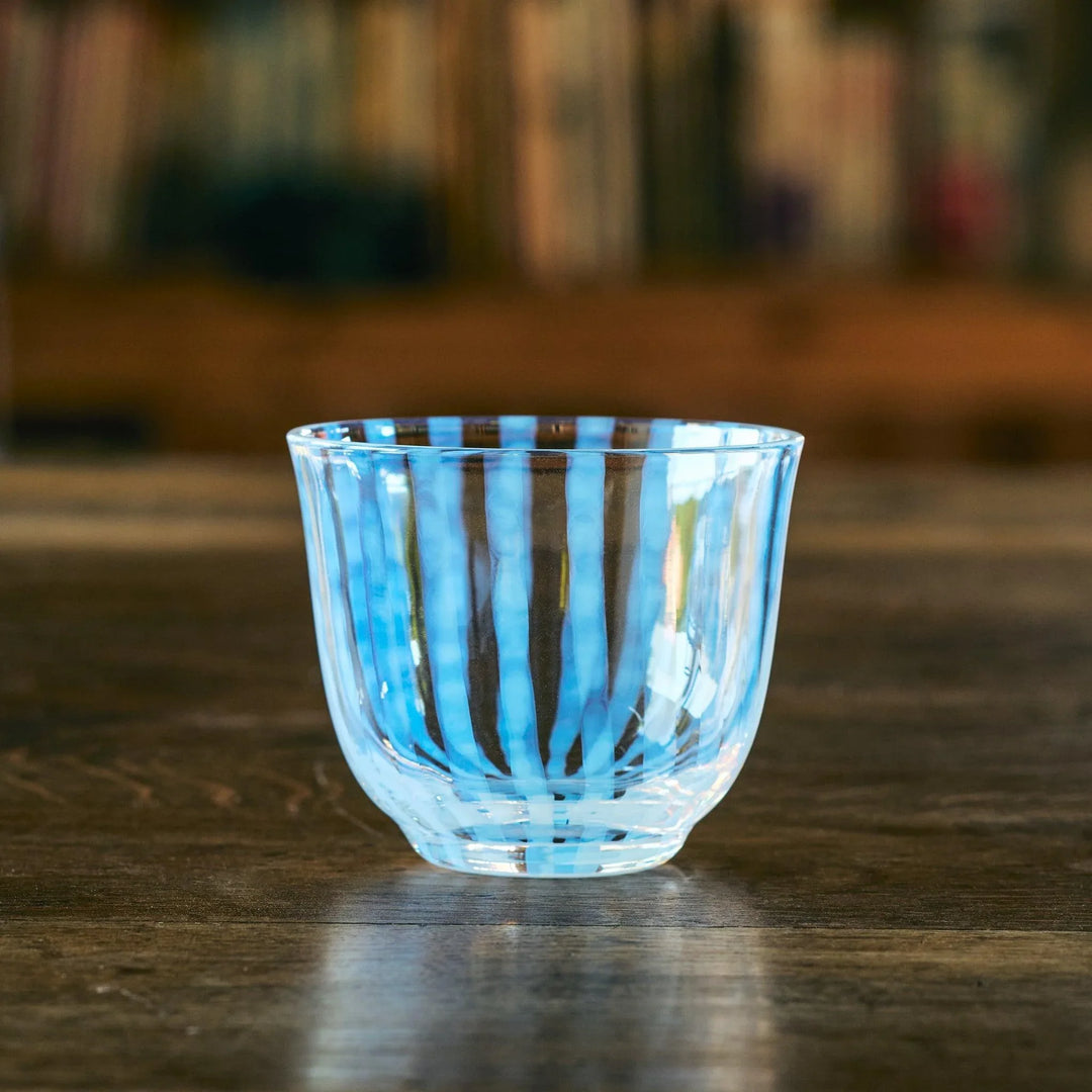 An empty Japanese glass tea cup with soft blue vertical stripes, set on a wooden table with a warm background.