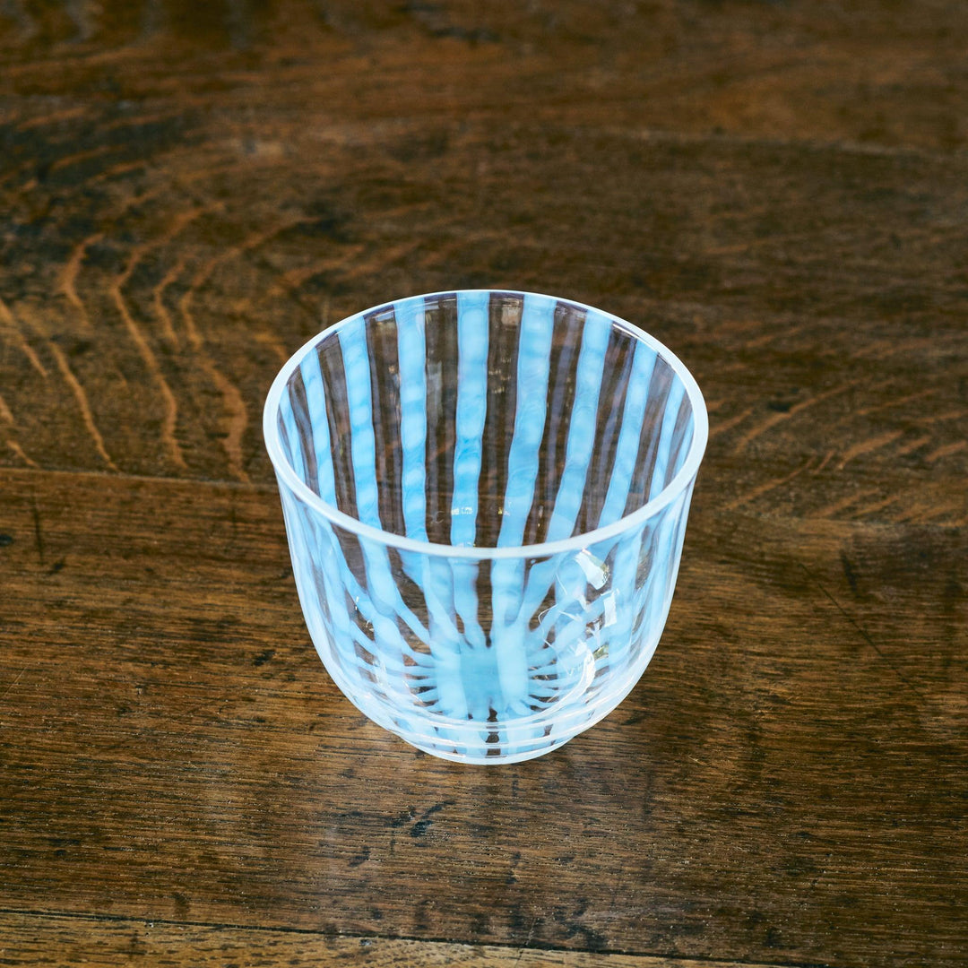 Top-angled view of a glass tea cup with hand-painted blue vertical lines, placed on rustic wood surface.