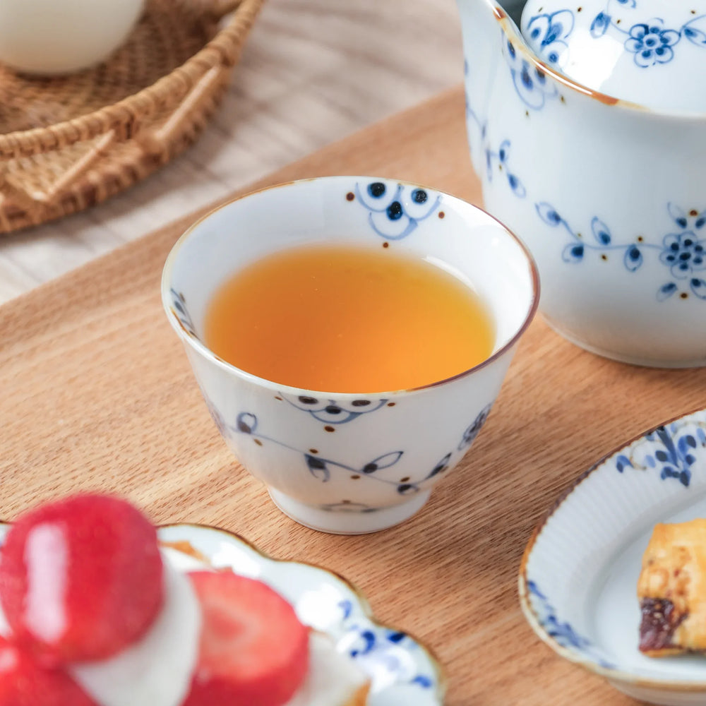 Japanese teacup with blue vine flower motifs, filled with tea and placed next to a dessert plate.