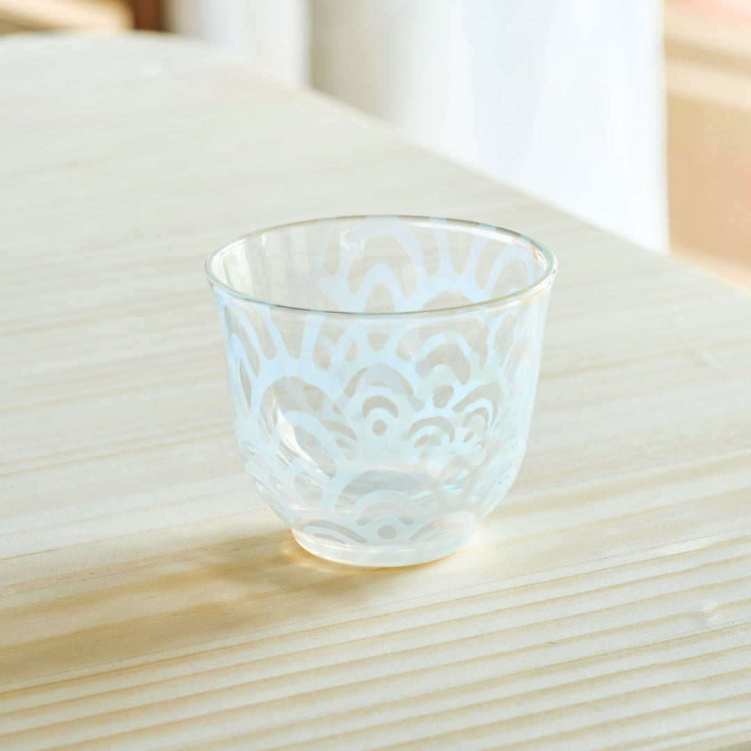Vintage Japanese glass tea cup with white wave patterns on a natural wooden table in bright morning sunlight
