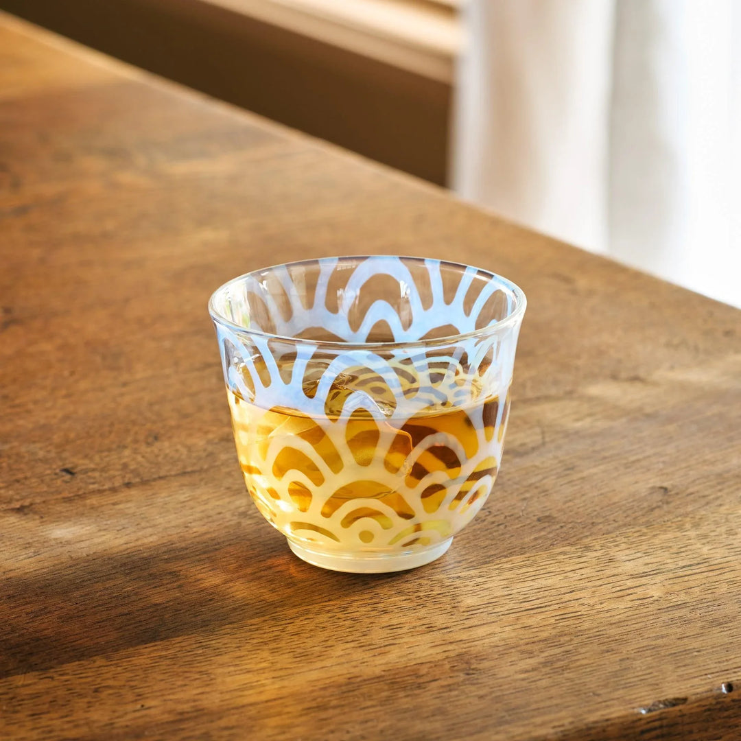 A vintage glass tea cup with a light blue art deco pattern, filled with amber tea, placed on a wooden table.