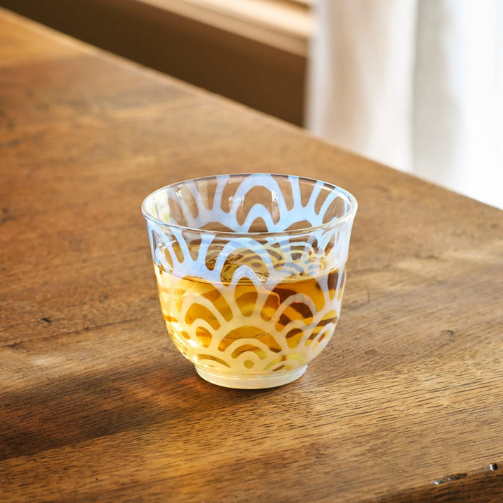 A vintage glass tea cup with a light blue art deco pattern, filled with amber tea, placed on a wooden table.