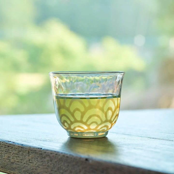 Japanese glass tea cup with blue Seigaiha patterns, filled with green tea and set by a sunlit window.