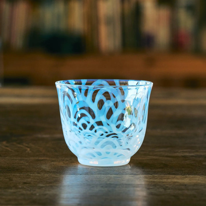 Empty Japanese glass tea cup with bold blue Seigaiha wave patterns, resting on a wooden table indoors.