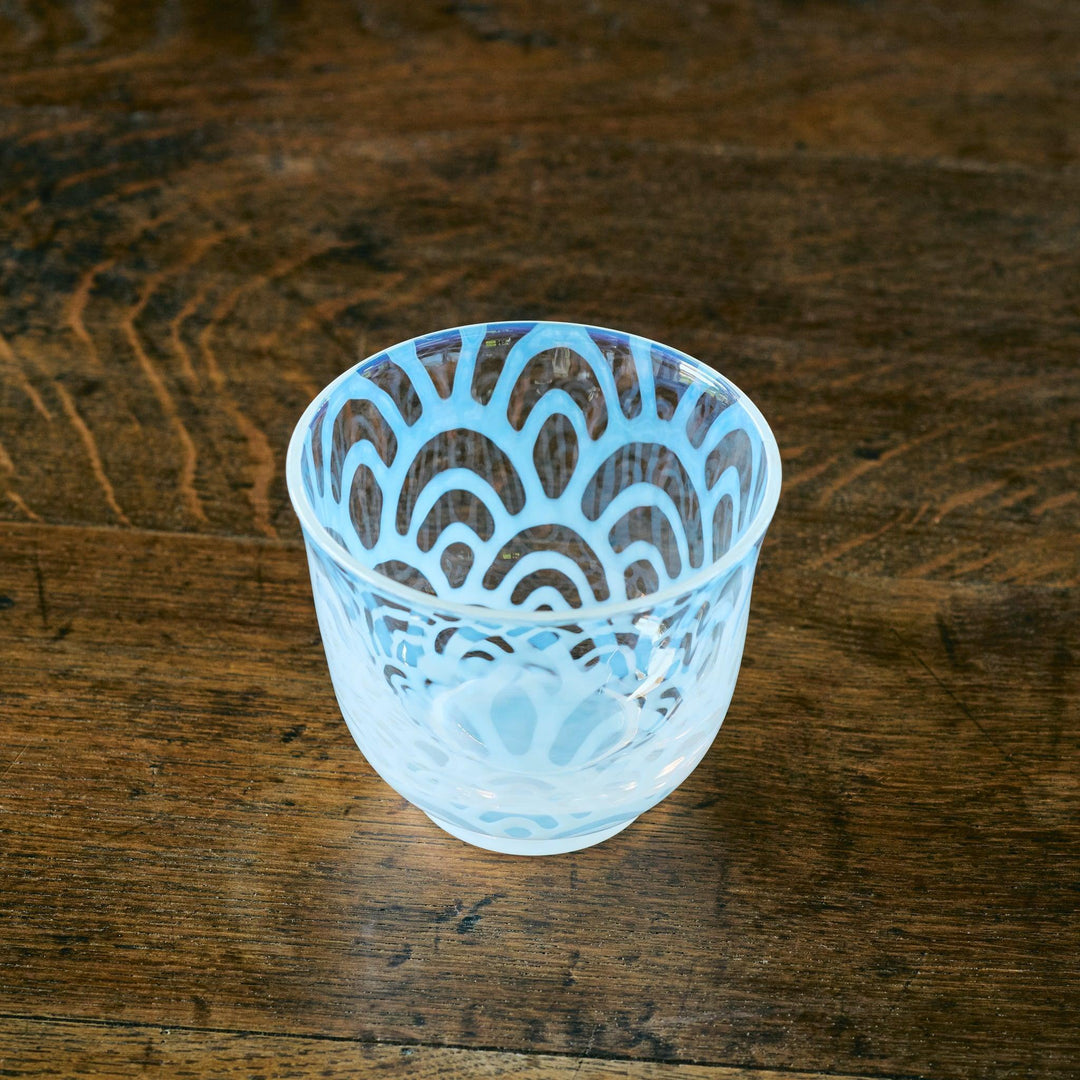 A Japanese glass tea cup featuring a pale blue Seigaiha wave pattern, resting on a rustic wooden table.