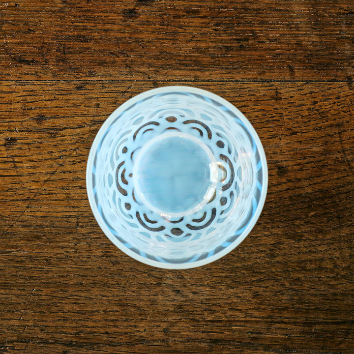 Top-down view of a glass tea cup with soft blue Seigaiha-style interior pattern, placed on a wooden surface.