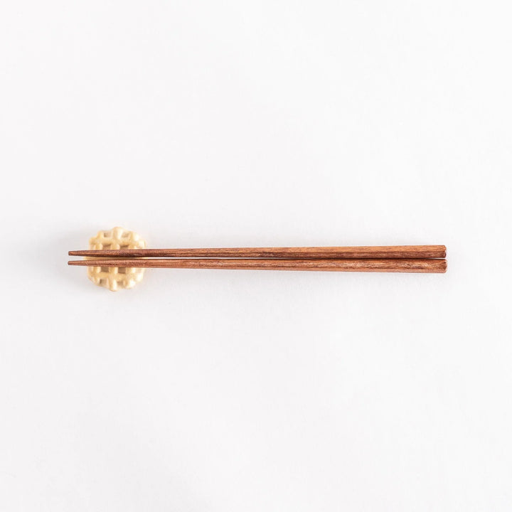 Waffle-shaped ceramic chopsticks rest with wooden chopsticks resting across it.