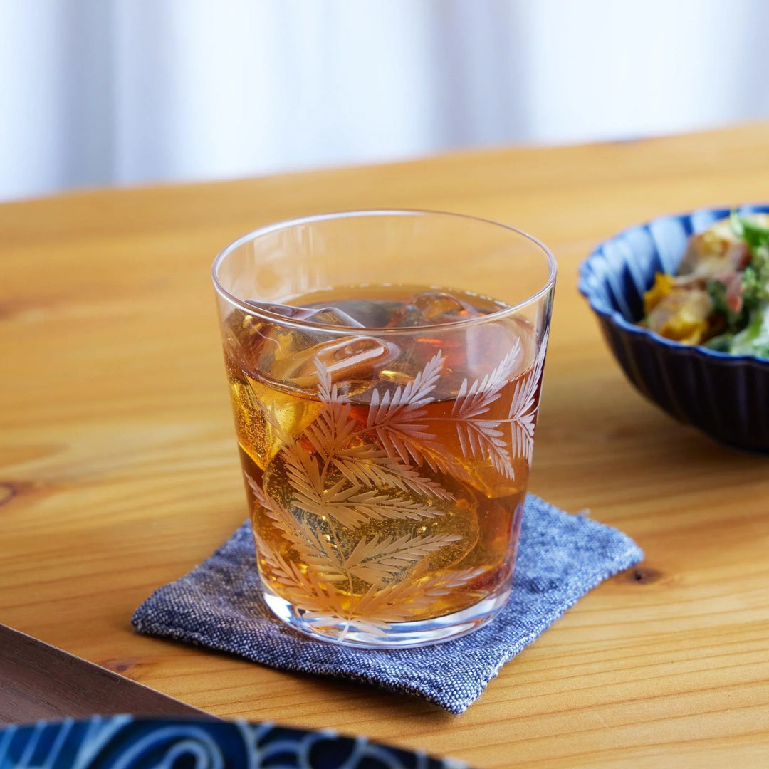 Japanese whiskey glass with etched fern leaf design, filled with iced tea and ice cubes, placed on a natural wood table.