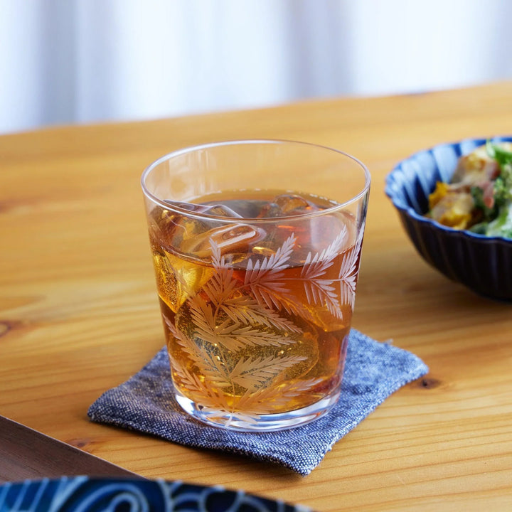 Japanese whiskey glass with etched fern leaf design, filled with iced tea and ice cubes, placed on a natural wood table.