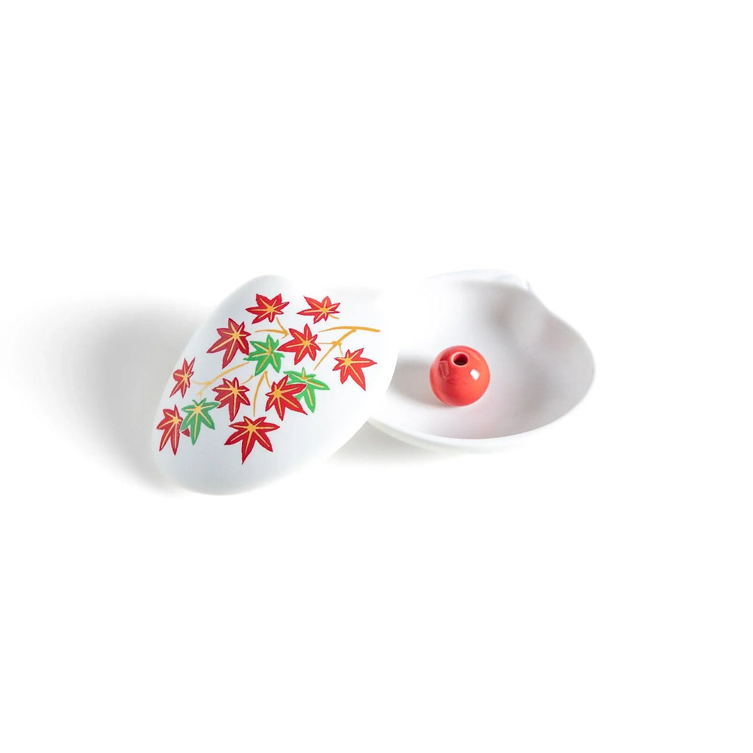 White seashell-shaped ceramic incense holder with red and green maple leaves and small red holder for incense.
