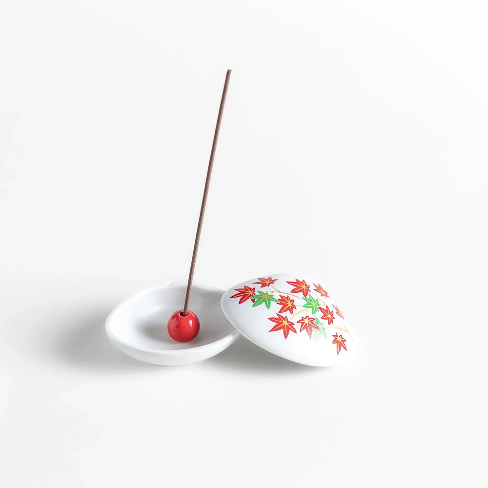 White seashell-shaped ceramic incense holder with red and green maple leaves and small red holder for incense.