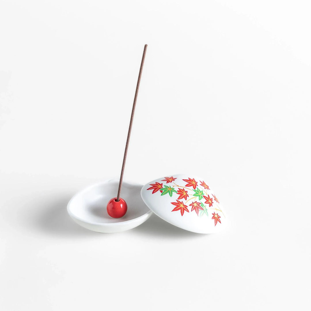 White seashell-shaped ceramic incense holder with red and green maple leaves and small red holder for incense.