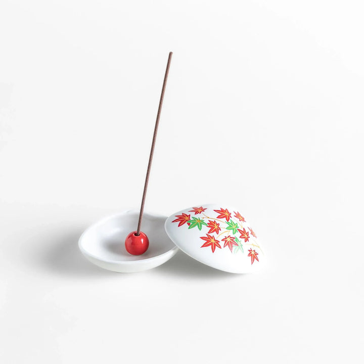 White seashell-shaped ceramic incense holder with red and green maple leaves and small red holder for incense.