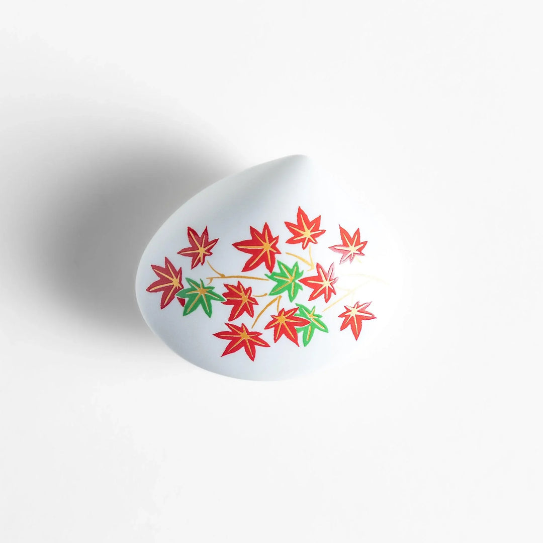 White seashell-shaped ceramic incense holder with red and green maple leaves and small red holder for incense.