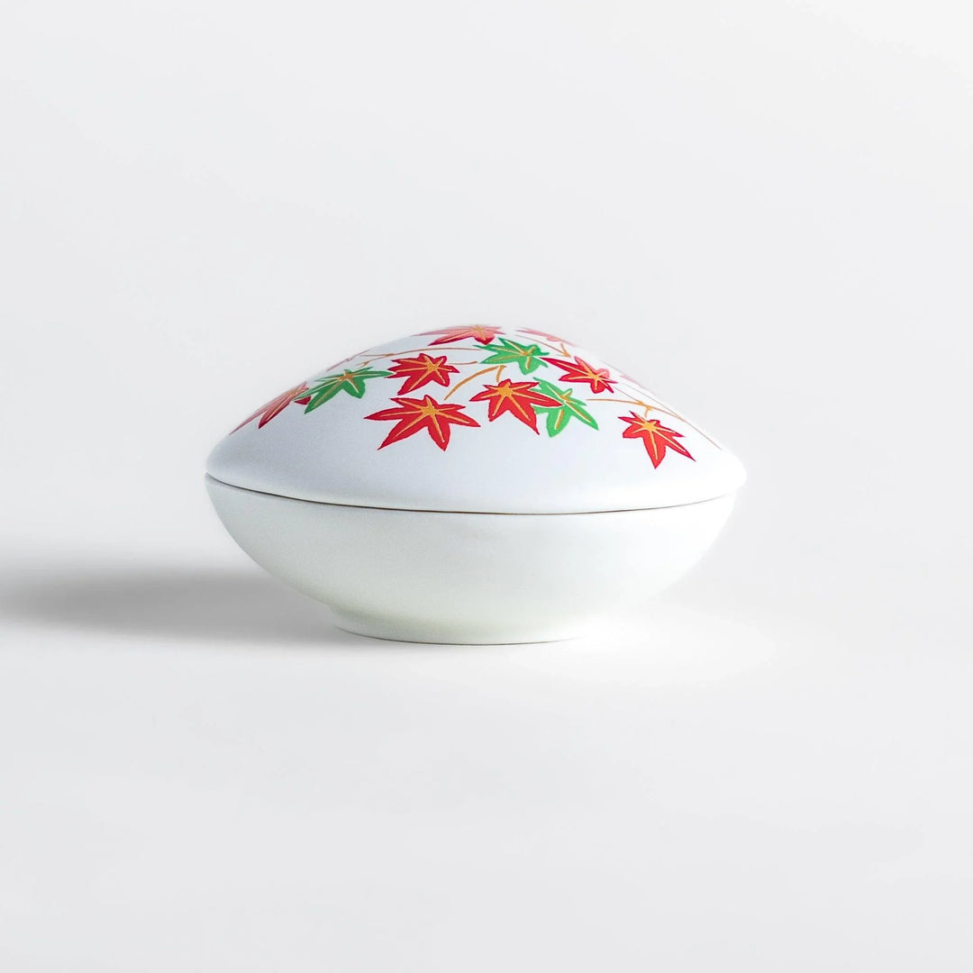 White seashell-shaped ceramic incense holder with red and green maple leaves and small red holder for incense.