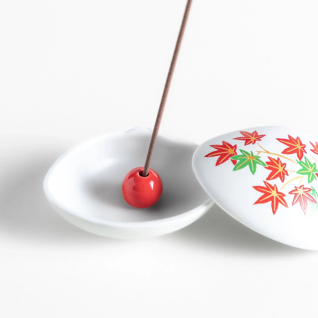 White seashell-shaped ceramic incense holder with red and green maple leaves and small red holder for incense.