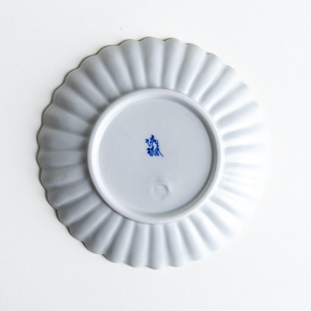 A smaller white porcelain plate with a fluted design, reminiscent of a chrysanthemum flower.