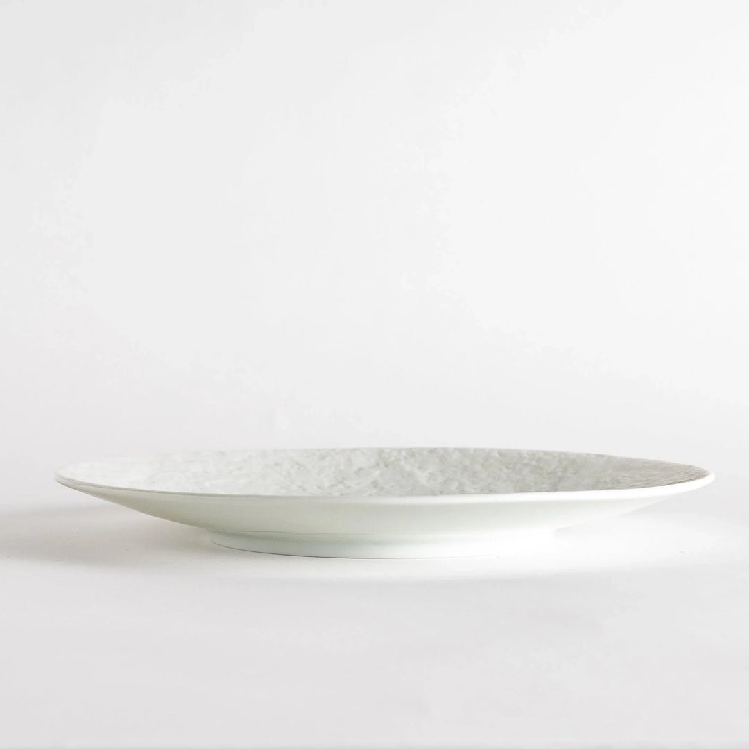 A white luncheon plate featuring a slightly irregular, organic texture and shape, providing a minimalist and natural look.