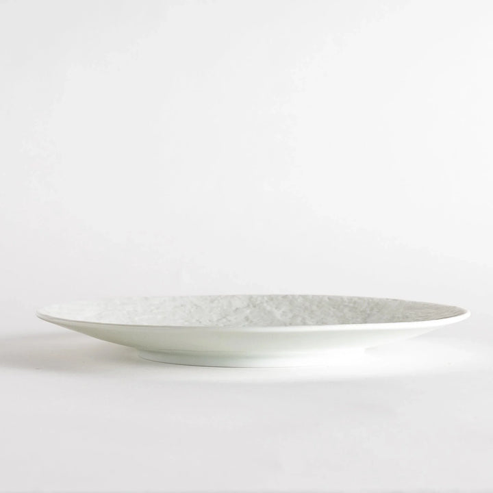 A white luncheon plate featuring a slightly irregular, organic texture and shape, providing a minimalist and natural look.