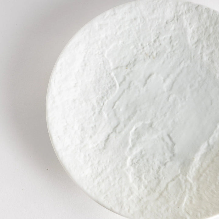 A white luncheon plate featuring a slightly irregular, organic texture and shape, providing a minimalist and natural look.