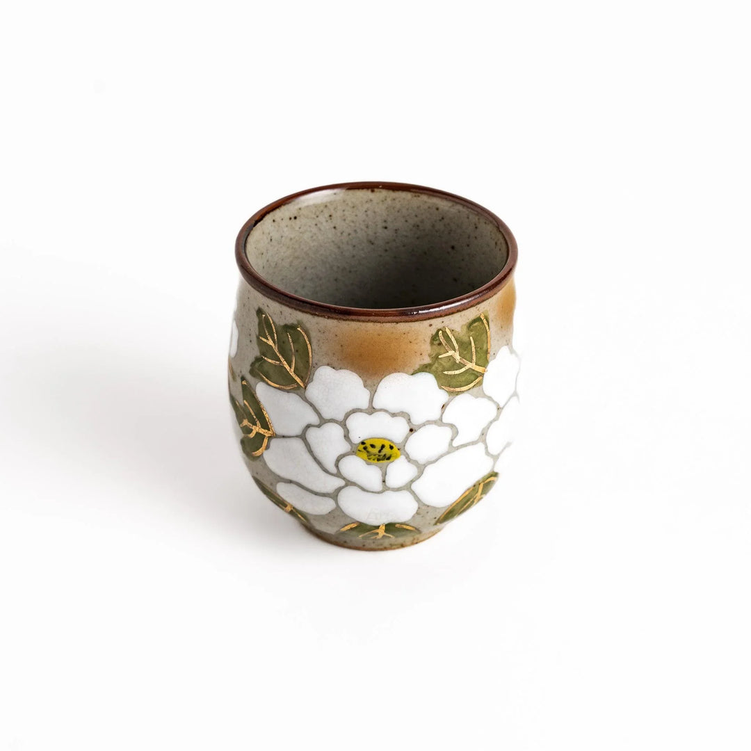 Ceramic teacup with a delicate white flower design and green leaves, perfect for enjoying a peaceful moment with tea.