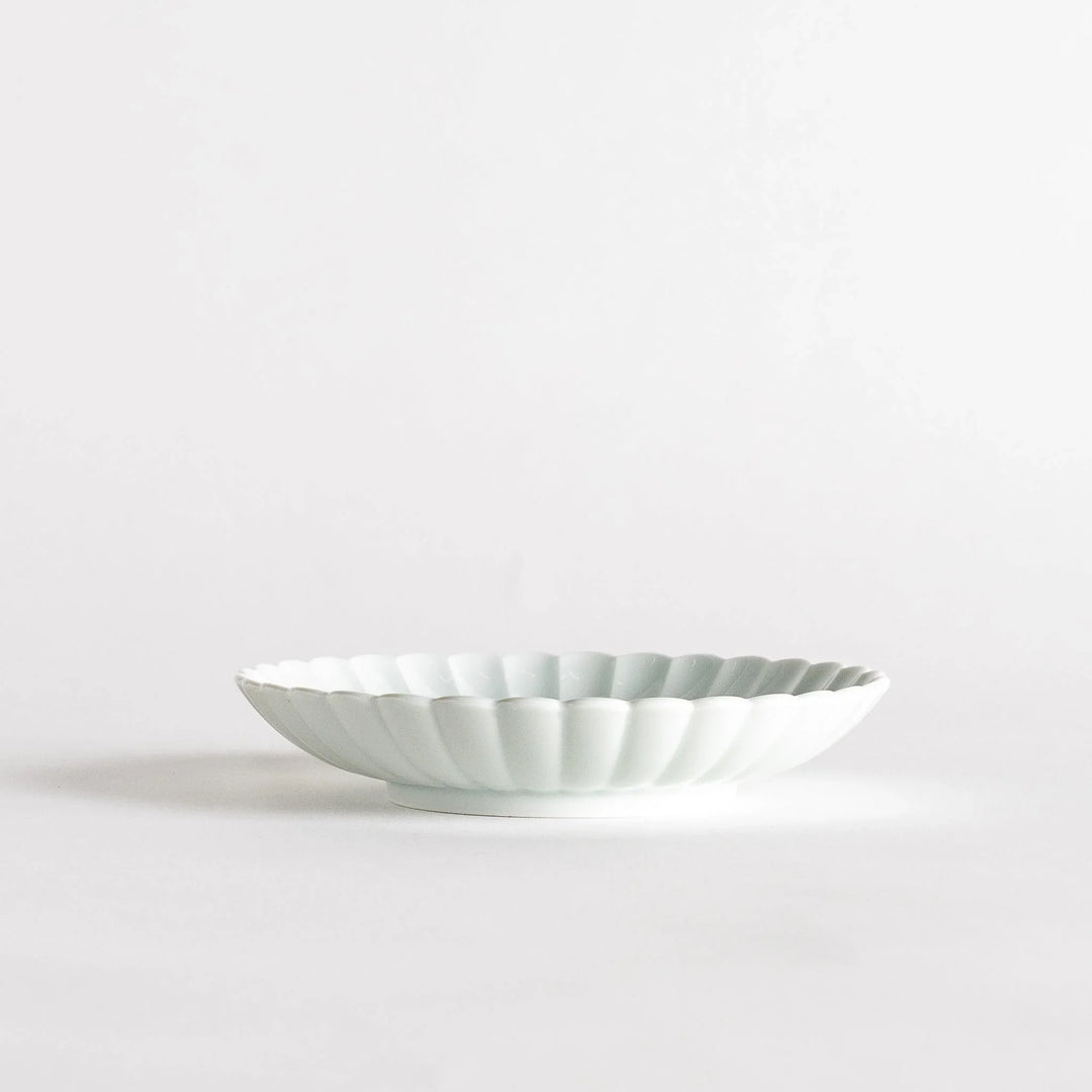 A simple white ceramic plate with a scalloped edge and a clean, minimalist design.