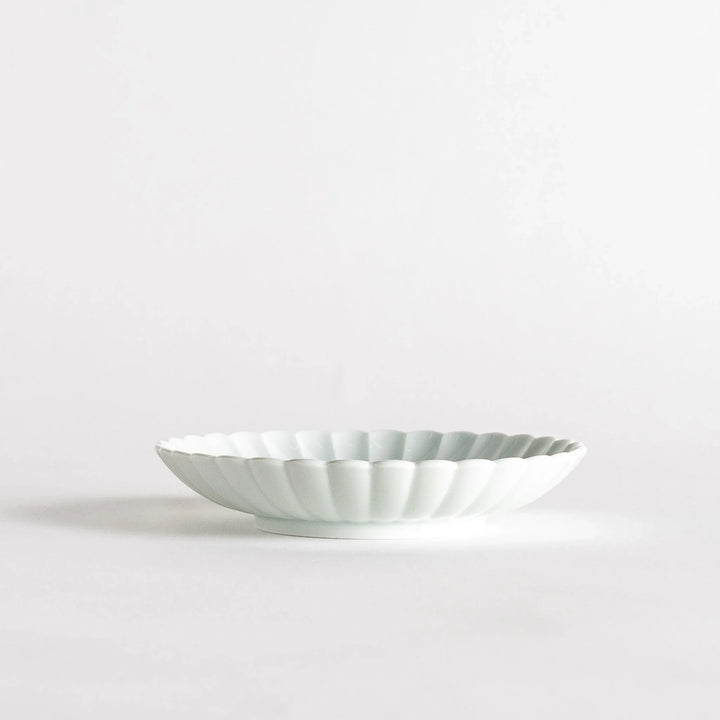 A simple white ceramic plate with a scalloped edge and a clean, minimalist design.