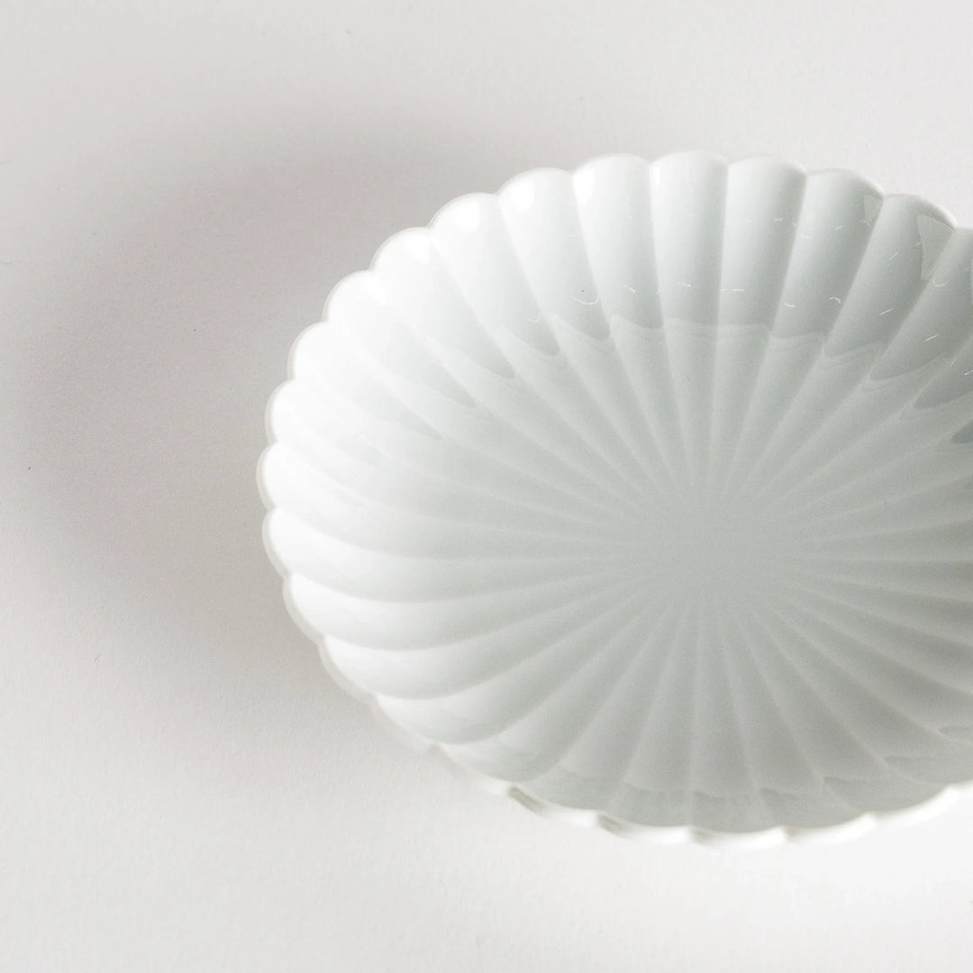 A simple white ceramic plate with a scalloped edge and a clean, minimalist design.