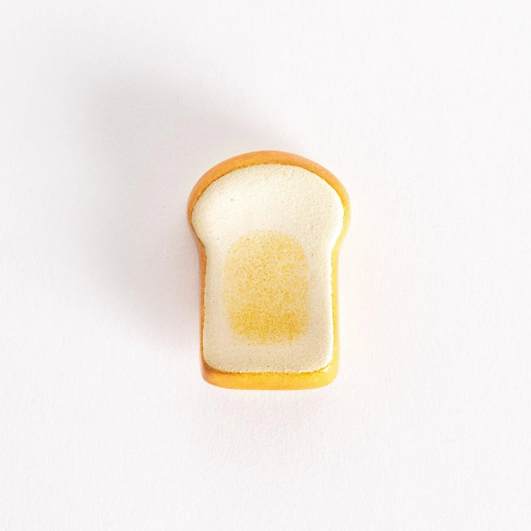A ceramic chopsticks rest shaped like a slice of toasted bread, featuring a golden-brown edge and soft white center.