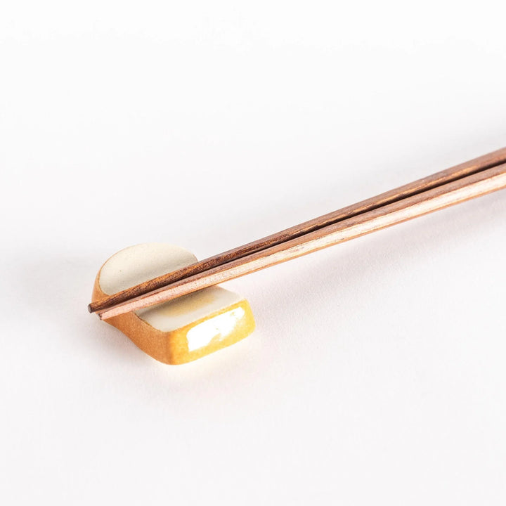 A close-up of the toast-shaped chopsticks rest with chopsticks placed across its surface.