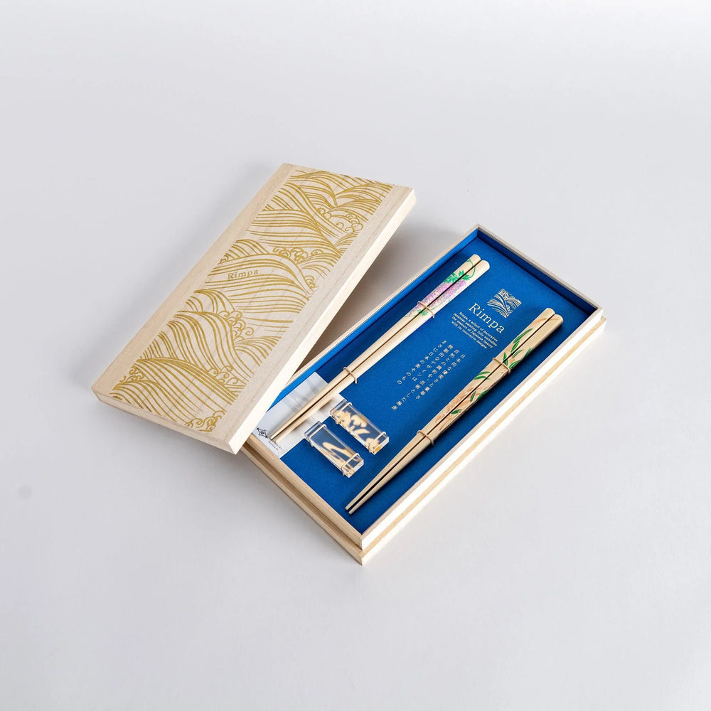 Elegant chopsticks with wisteria and bamboo motifs in wooden box with blue background for gifting.