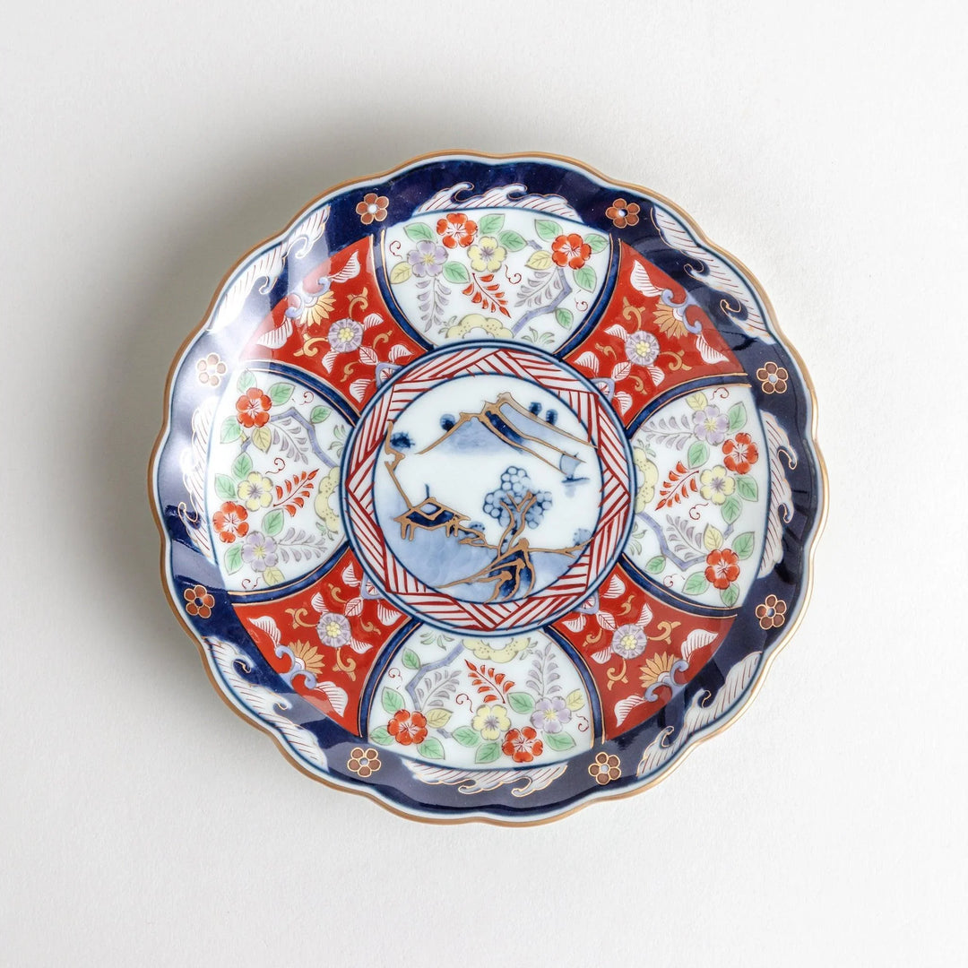 Small scalloped porcelain bowl with Imari style decoration central landscape and red blue rim motifs.