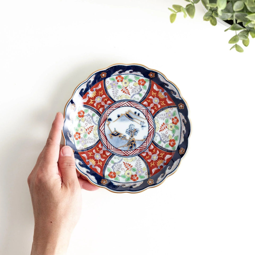 Small scalloped porcelain bowl with Imari style decoration central landscape and red blue rim motifs.