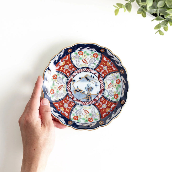 Small scalloped porcelain bowl with Imari style decoration central landscape and red blue rim motifs.