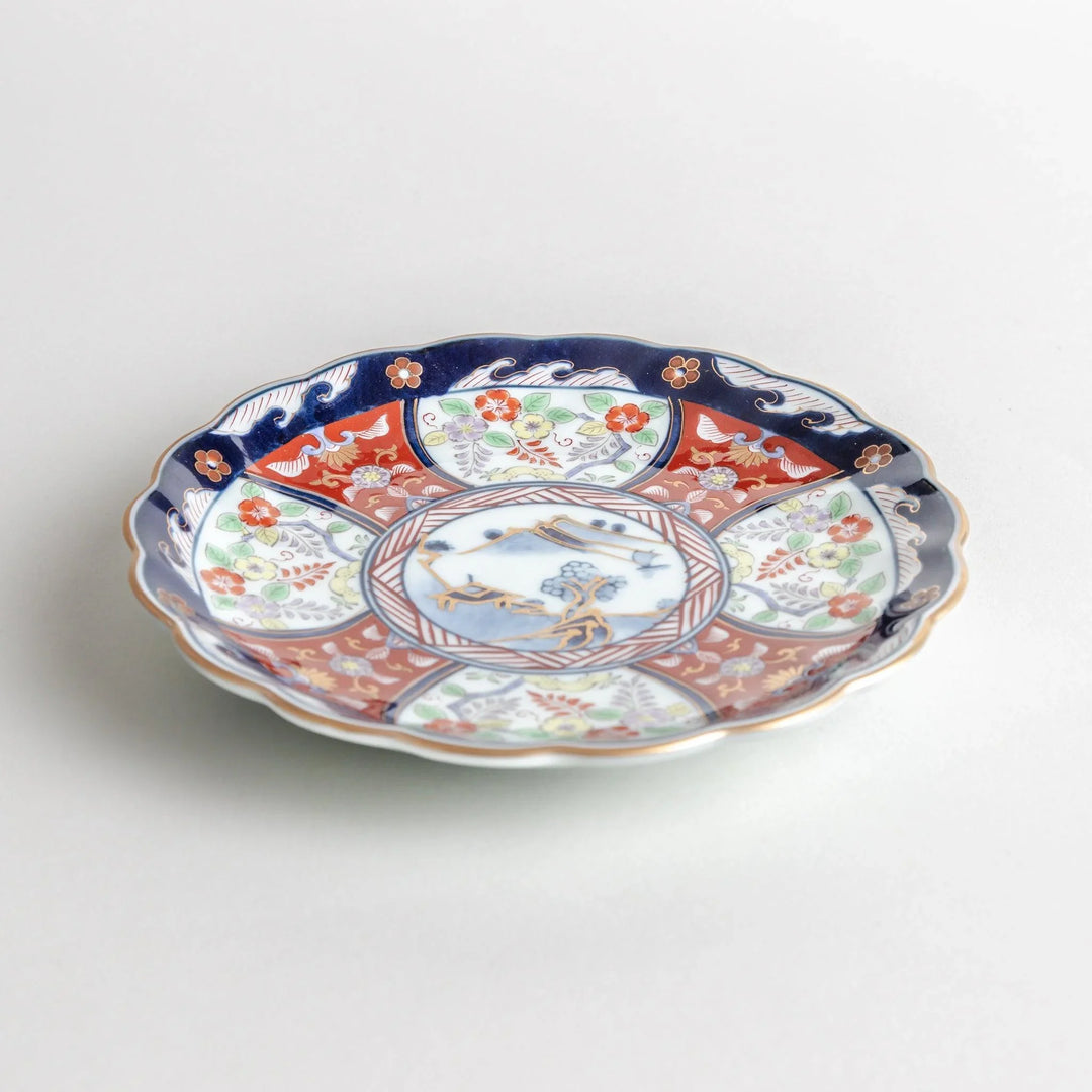 Small scalloped porcelain bowl with Imari style decoration central landscape and red blue rim motifs.