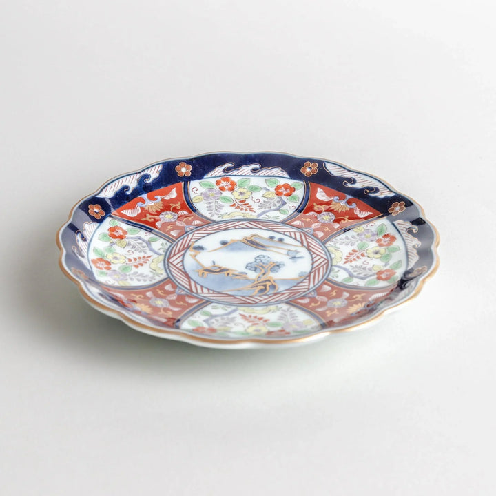 Small scalloped porcelain bowl with Imari style decoration central landscape and red blue rim motifs.