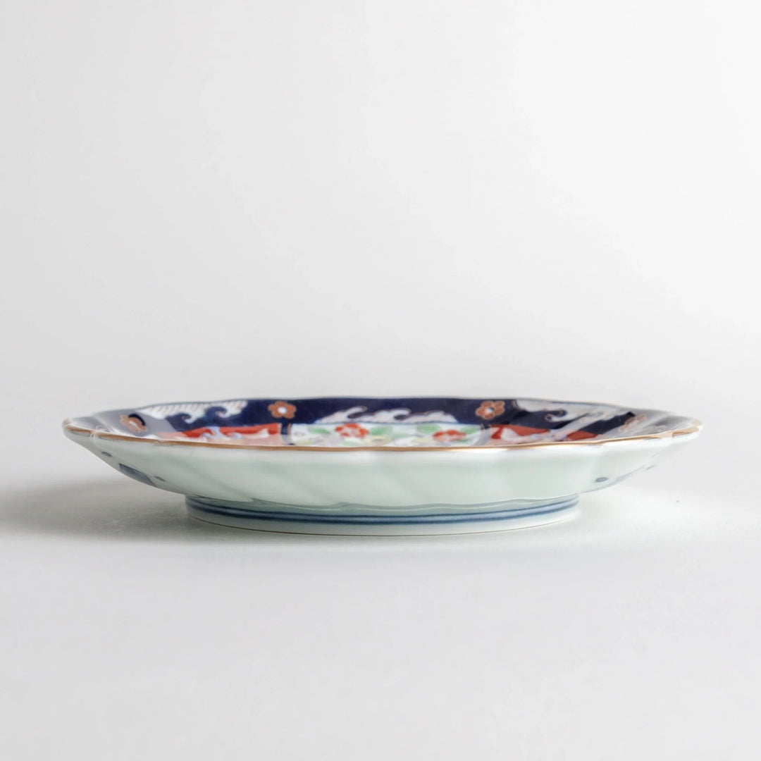 Small scalloped porcelain bowl with Imari style decoration central landscape and red blue rim motifs.