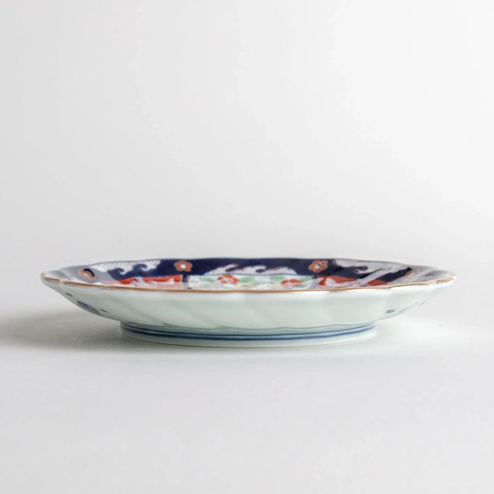 Small scalloped porcelain bowl with Imari style decoration central landscape and red blue rim motifs.