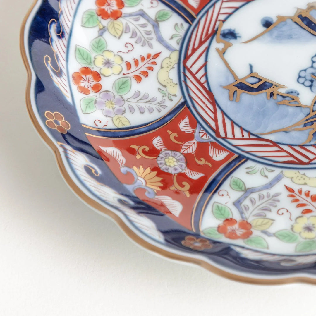 Small scalloped porcelain bowl with Imari style decoration central landscape and red blue rim motifs.