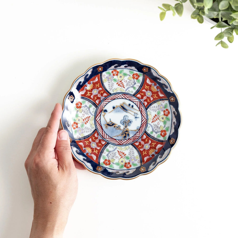 Scalloped porcelain bowl with Imari style red and blue alternating patterns and central landscape motif.