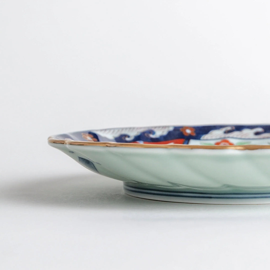 Scalloped porcelain bowl with Imari style red and blue alternating patterns and central landscape motif.