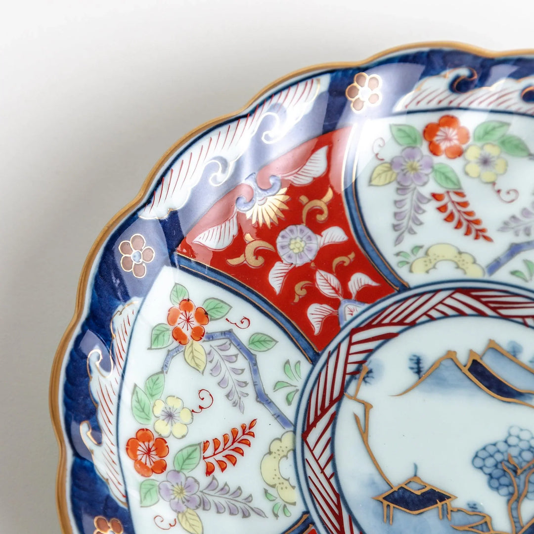 Scalloped porcelain bowl with Imari style red and blue alternating patterns and central landscape motif.