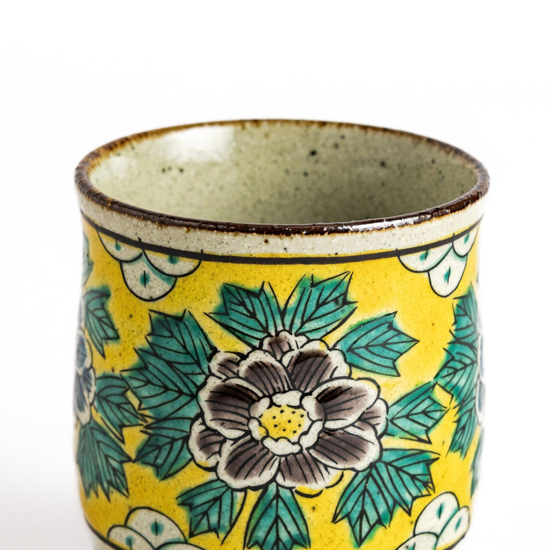 Yellow ceramic teacup with a beautiful floral pattern, featuring a brown rim and a unique base design.