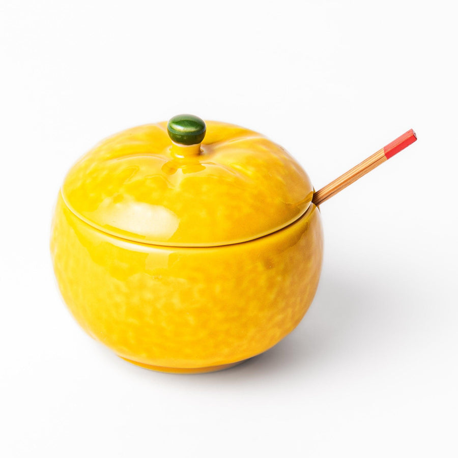 A small ceramic container shaped like a yuzu fruit with a lid and a spoon, bright yellow color.