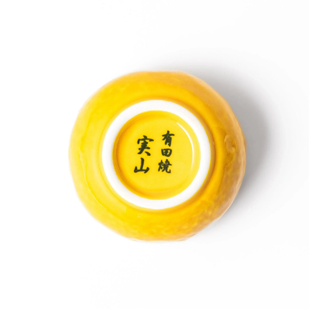 A small ceramic container shaped like a yuzu fruit with a lid and a spoon, bright yellow color.