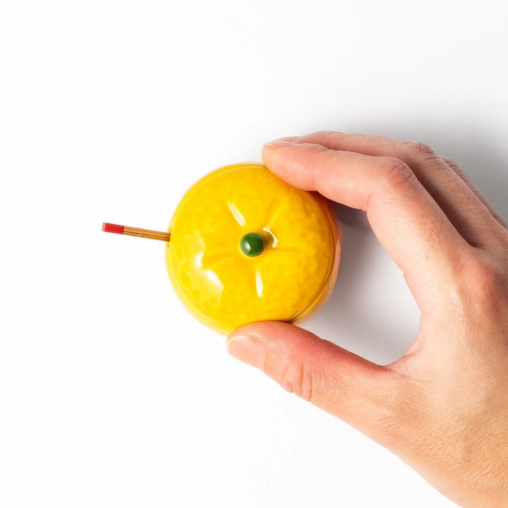 A small ceramic container shaped like a yuzu fruit with a lid and a spoon, bright yellow color.