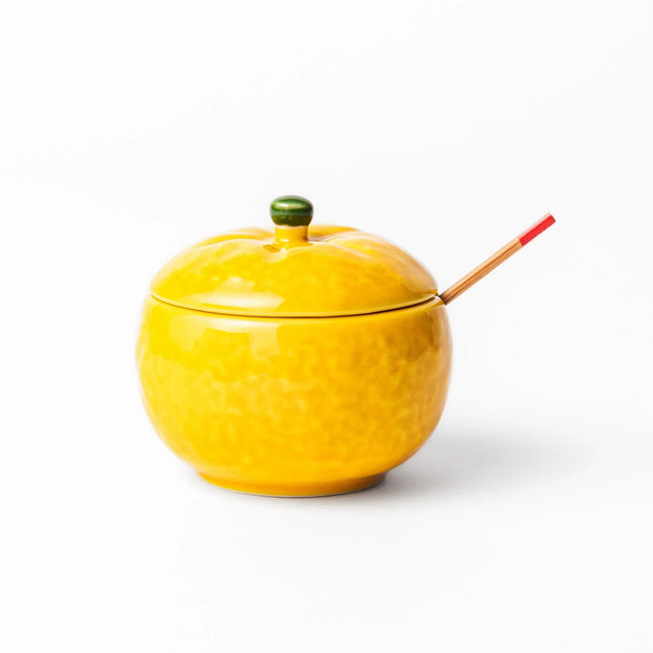 A small ceramic container shaped like a yuzu fruit with a lid and a spoon, bright yellow color.