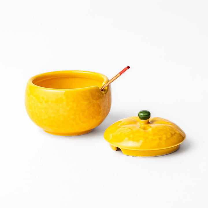 A small ceramic container shaped like a yuzu fruit with a lid and a spoon, bright yellow color.