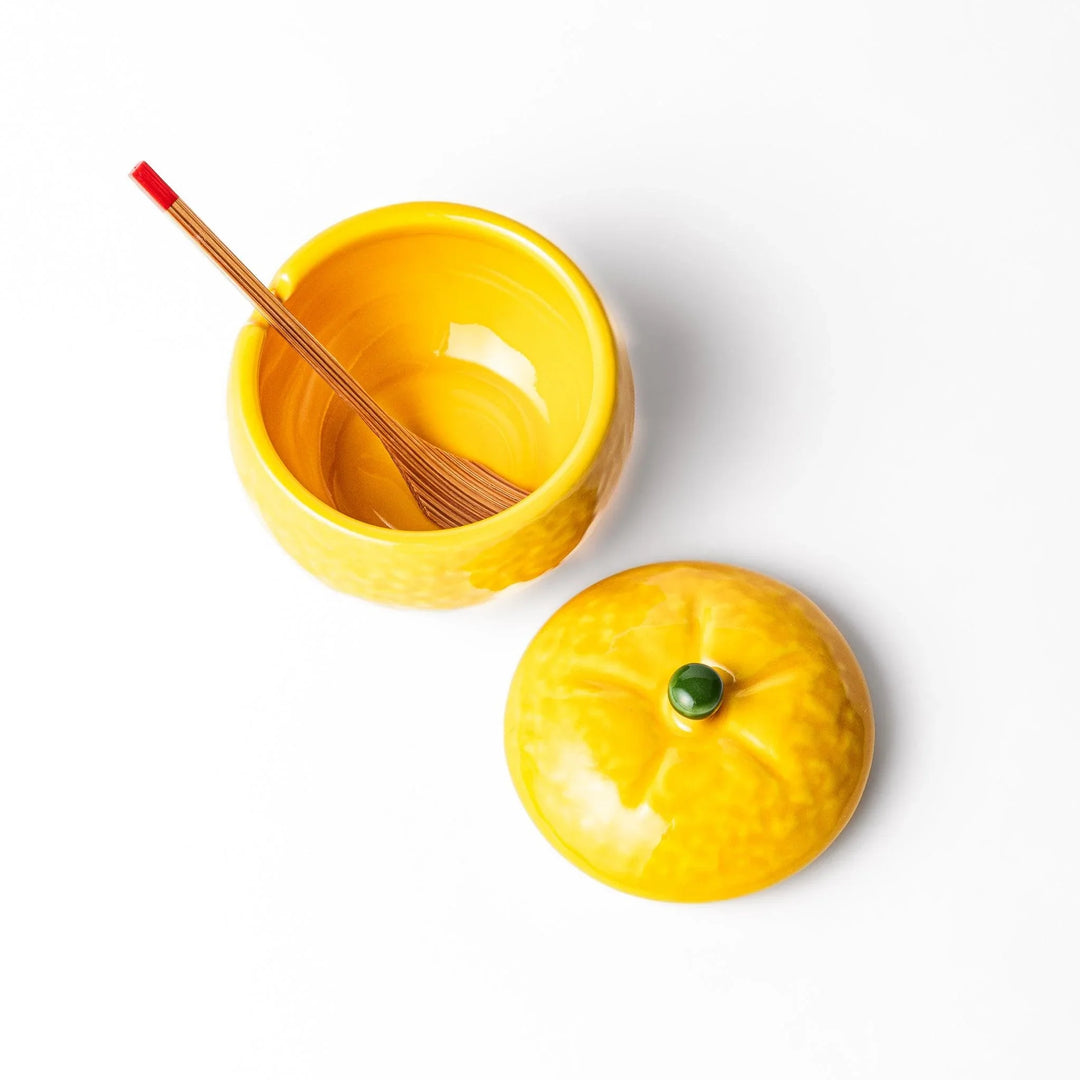 A small ceramic container shaped like a yuzu fruit with a lid and a spoon, bright yellow color.