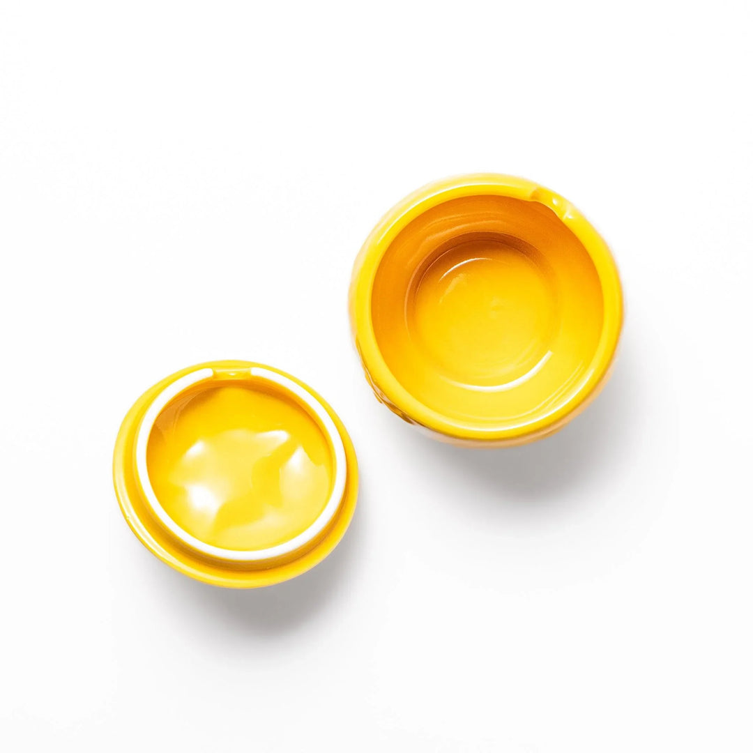 A small ceramic container shaped like a yuzu fruit with a lid and a spoon, bright yellow color.